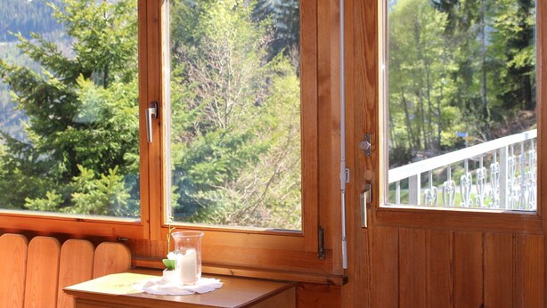 Une fenêtre à cadre en bois donnant sur une forêt et des montagnes.