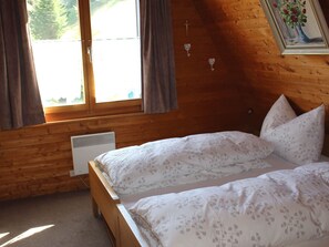 A bedroom with two beds, a window with curtains, a radiator, and a framed picture on the wall. - Chalet Iris, (Flumserberg Tannenheim), by Interhome (Flumserberg Tannenheim)