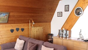 Une pièce confortable de style loft, avec un plafond en bois, un canapé agrémenté de coussins, une armoire en bois et une radio posée sur une table.