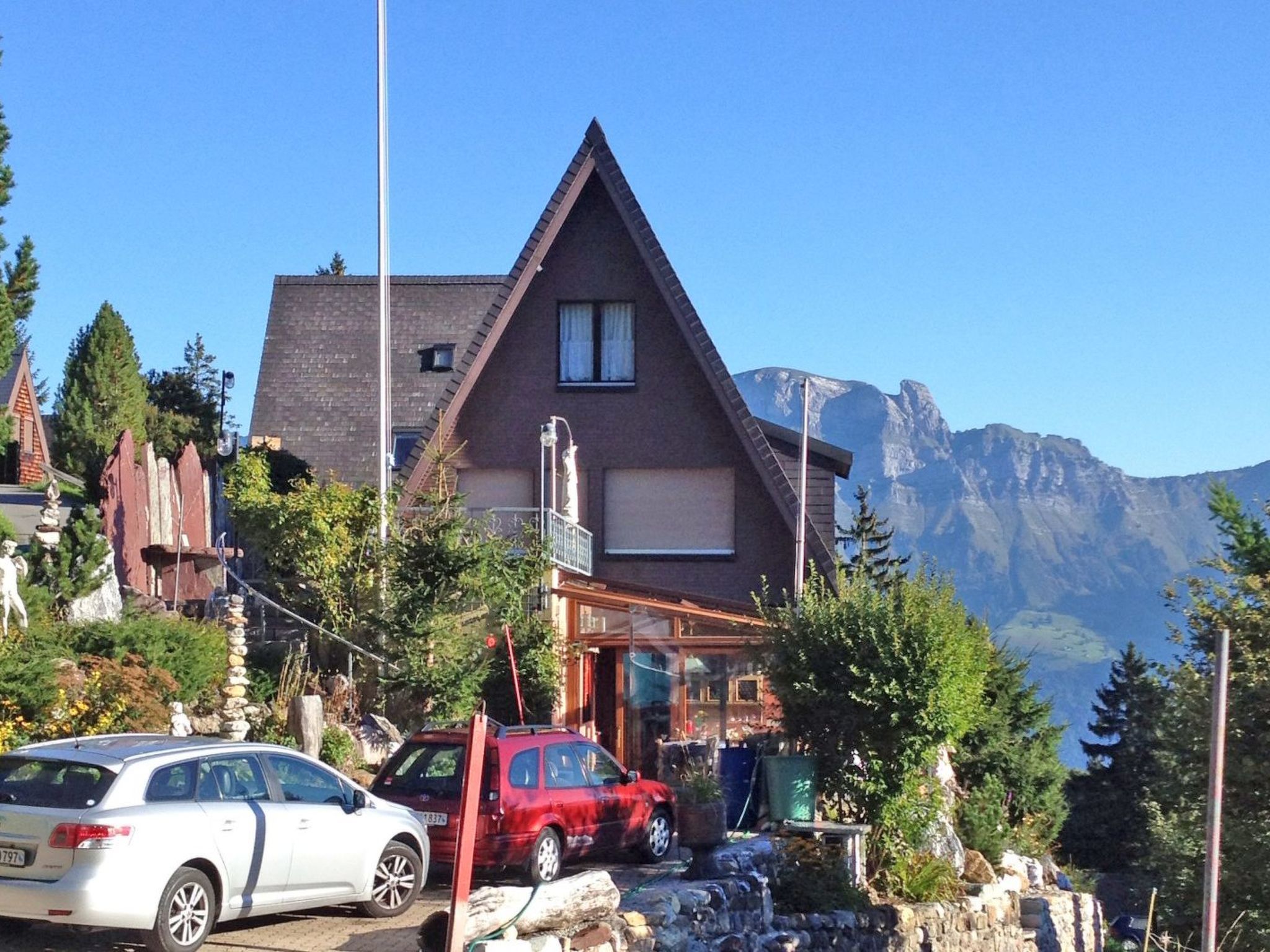 A two-story house with a sloped roof, a balcony, and a mountain backdrop.