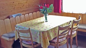 Un espace avec des bancs en bois et une table recouverte d’une nappe à motifs floraux, entouré de chaises en bois.
