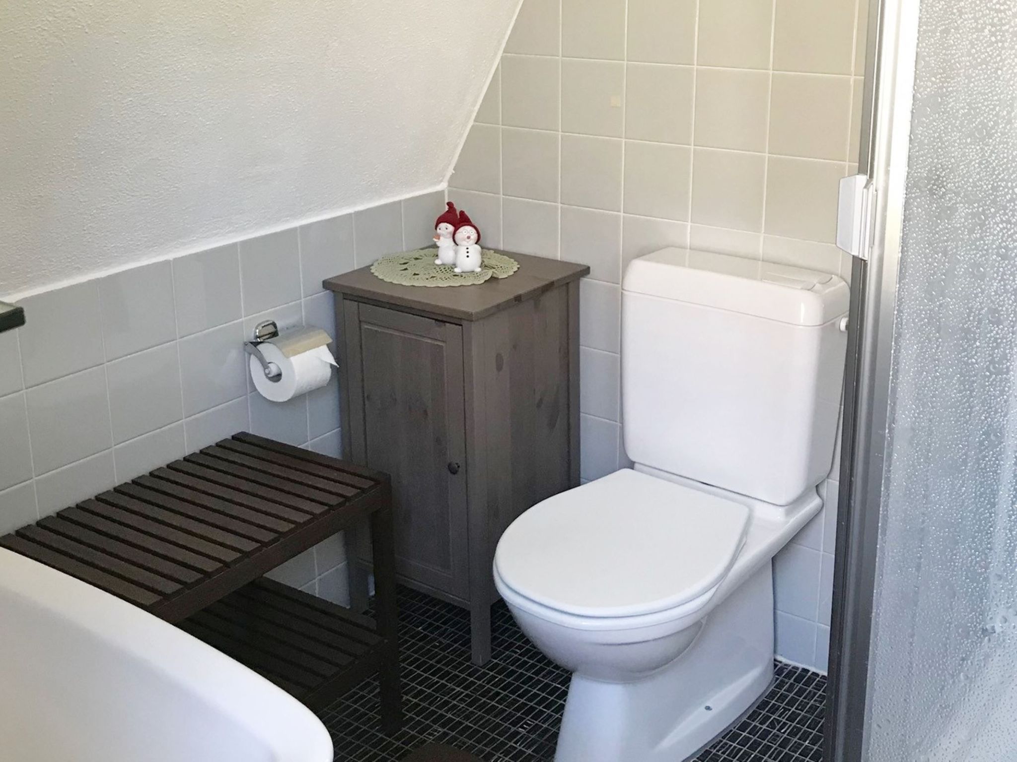 A small bathroom with a toilet, a wooden shelf, and a roll of toilet paper.