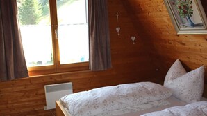 Une chambre avec deux lits, des murs en bois, une fenêtre avec des rideaux, un radiateur et un tableau encadré accroché au mur.