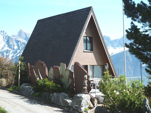 Un chalet de montagne doté d’un toit à forte pente, de grandes fenêtres et offrant une vue sur des sommets enneigés.