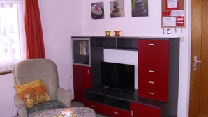 Ein Wohnzimmer mit einer Couch, einem Fernseher, einem kleinen Tisch und einem roten Schrank.