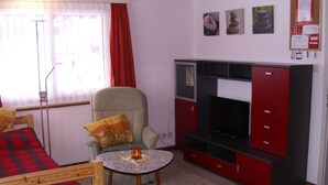 Ein Zimmer mit einem Bett, einem Sessel, einem kleinen Tisch mit Kerze, einem Fernseher und einem Schrank.