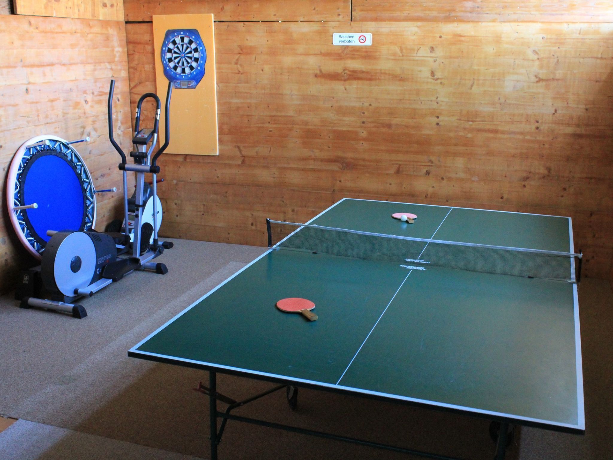 Taula de ping-pong amb dues paletes i un joc de daus en una habitació amb parets de fusta.