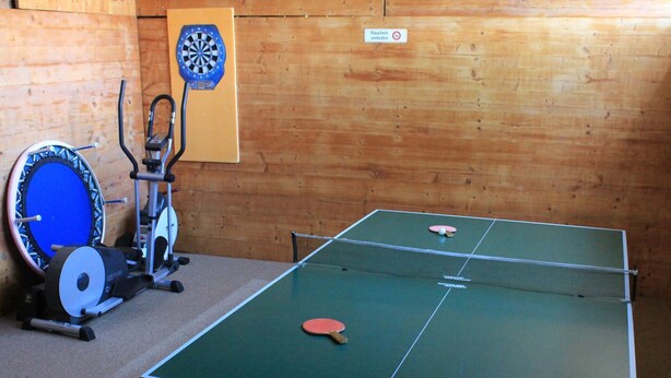 Ein Tischtennistisch mit zwei Schlägern und einer Dartscheibe in einem Raum mit Holzwänden.