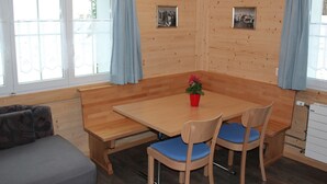 Ein Holzinnenraum mit einem Esstisch, zwei Stühlen, einer Bank und einem Sofa.