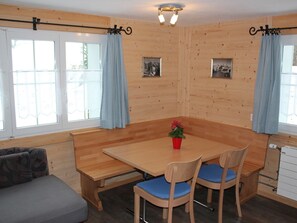 Ein Holzinnenraum mit einem Esstisch, zwei Stühlen, einer Bank und einem Sofa.