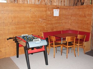 A foosball table and a red table with four wooden chairs in a room with wooden walls. - Chalet Good, (Flumserberg Tannenheim), by Interhome (Flumserberg Tannenheim)