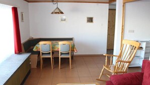 Une pièce comprenant une table à manger, deux chaises, un fauteuil à bascule, un canapé rouge, un sol carrelé et un plafond en bois.