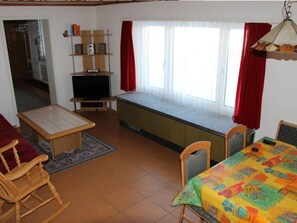 A room with a television, a bench, a dining table with chairs, and a window with curtains. - Haus Bernova, (Flumserberg Tannenboden), by Interhome (Flumserberg Tannenheim)