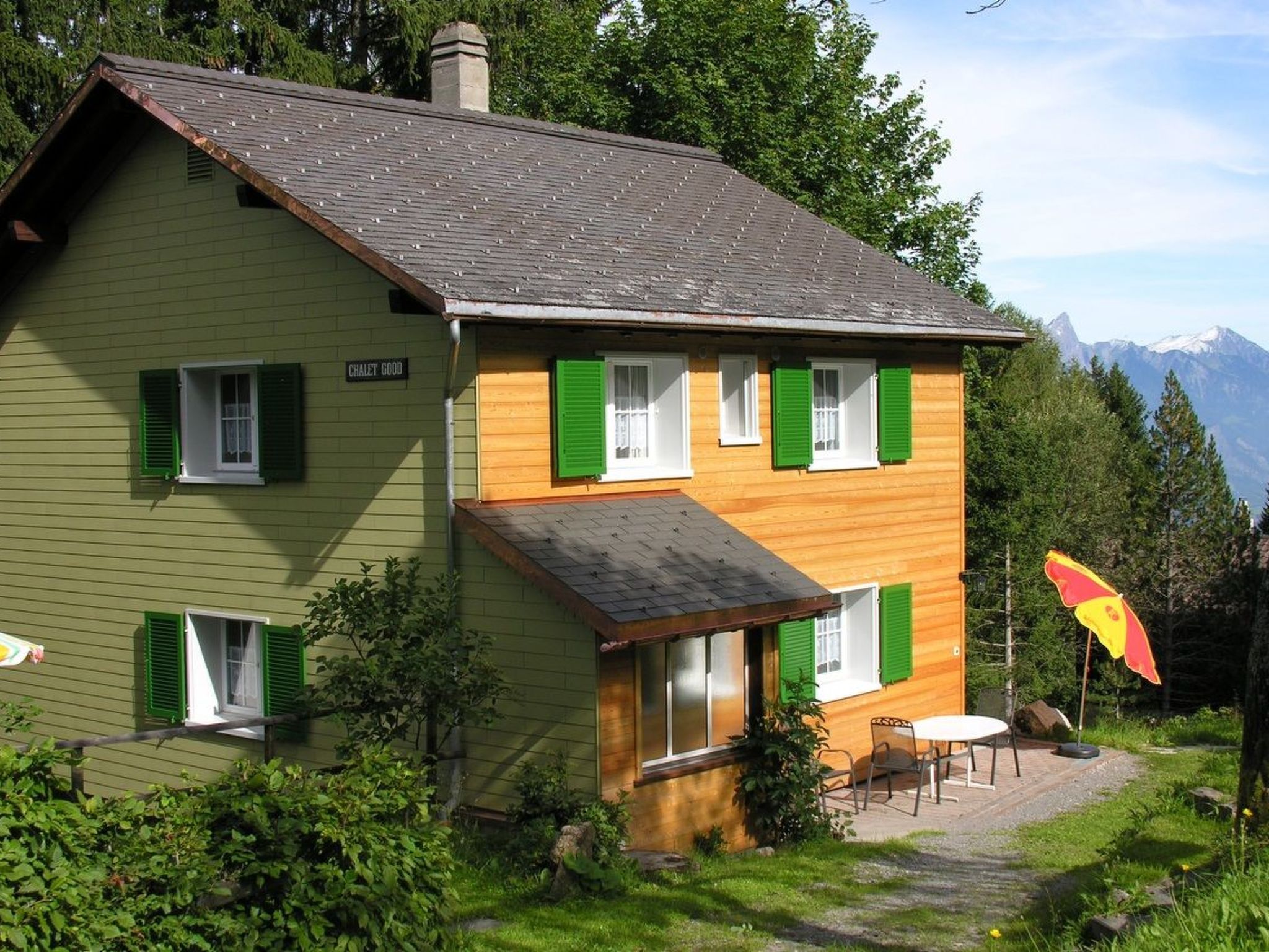 A two-story house with green shutters, a chimney, and a mountain view.