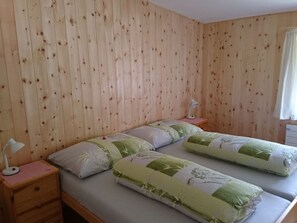 Ein Zimmer mit zwei Betten, Holzwänden, einem Nachttisch mit Lampe und einem Fenster mit Vorhängen.