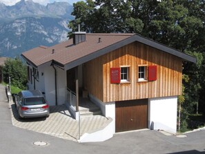 Ein zweigeschossiges Gebäude mit Garage, ein Auto davor und Blick auf einen Berg.