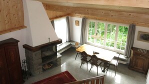 Habitació amb una xemeneia, una taula de dinar amb cadires, una finestra amb cortines i un sostre de fusta.