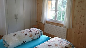 Habitació amb dos llits, un armari, una finestra amb cortines i un radiador.