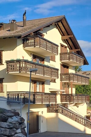 A multi-story building with balconies, a stone wall, and a clear sky.