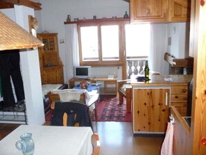 A compact kitchen with wooden cabinets, a dining area with a table and chairs, and a small TV.