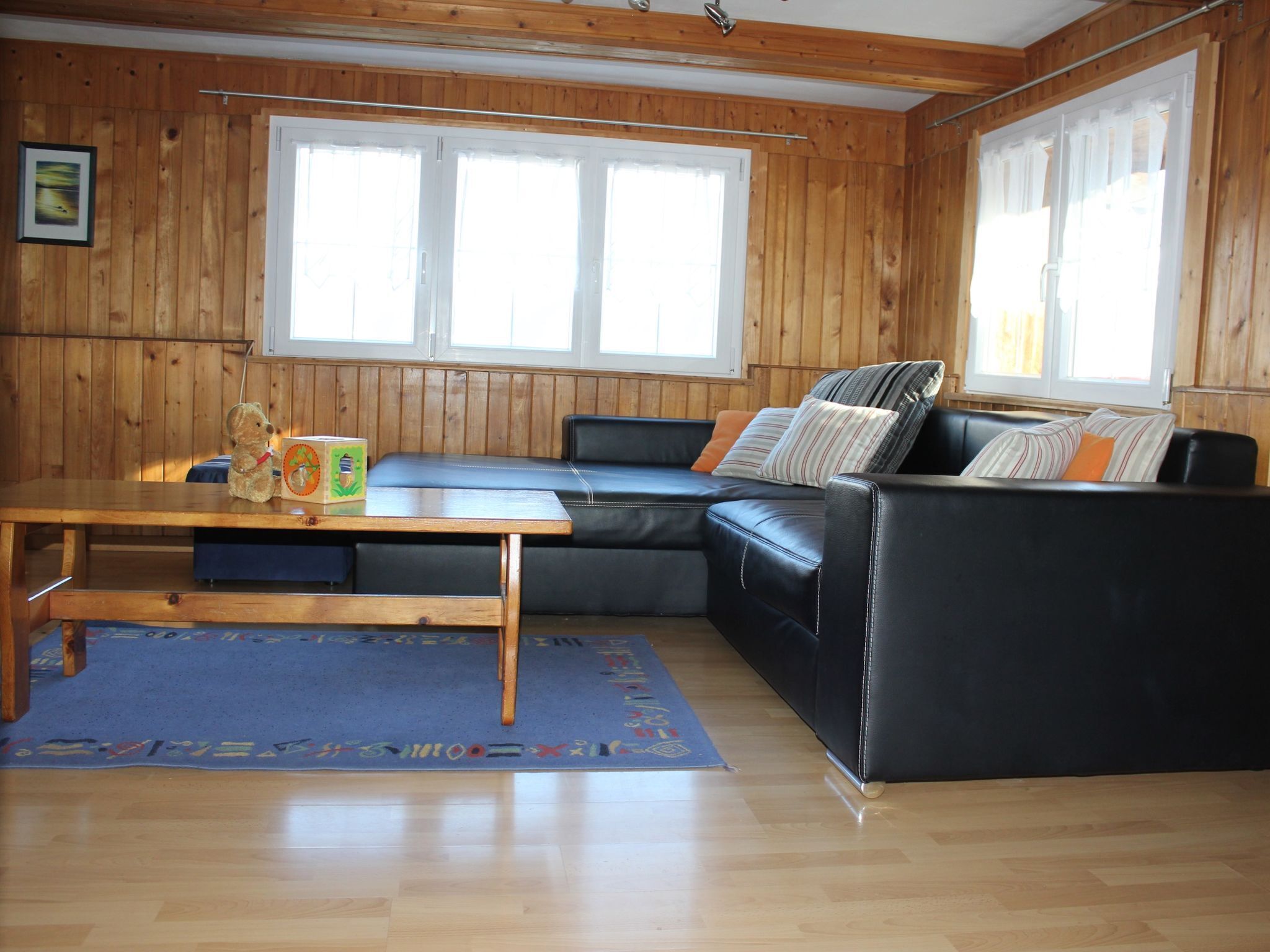 Une pièce aux murs en bois, avec un canapé en cuir noir, une table en bois et un tapis bleu.