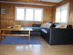 A room with wooden walls, a black leather sofa, a wooden table, and a blue rug. - Ferienhaus Fäsch, (Flumserberg Bergheim), by Interhome (Flumserberg Bergheim)