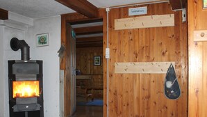Une pièce avec un poêle à bois, des murs en bois, une porte avec une pancarte et un porte-chaussures.