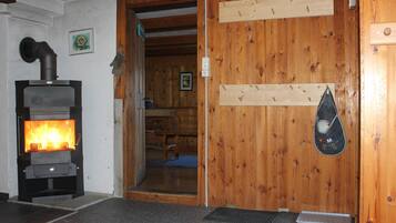 Une pièce avec un poêle à bois, des murs en bois, une porte avec une pancarte et un porte-chaussures.