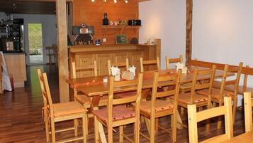 Un coin repas en bois avec une longue table et des chaises, une cuisine en arrière-plan et une vue sur l’extérieur.