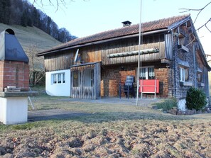 A two-story wooden house with a sloped roof, a brick chimney, and a small attached white building with a window. - Ferienhaus Fäsch, (Flumserberg Bergheim), by Interhome (Flumserberg Bergheim)