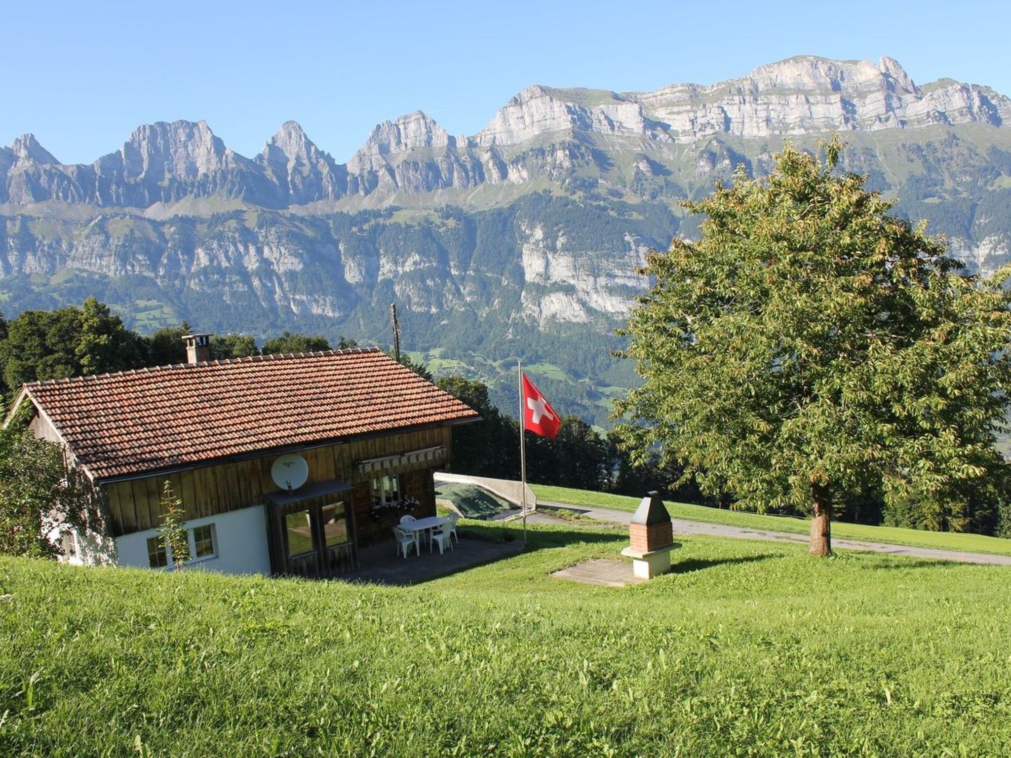 Ein Chalet mit rotem Ziegeldach, einer Schweizer Flagge und einer Bergkulisse.
