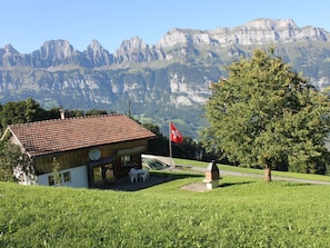 A chalet with a red-tiled roof, a Swiss flag, and a mountain backdrop.