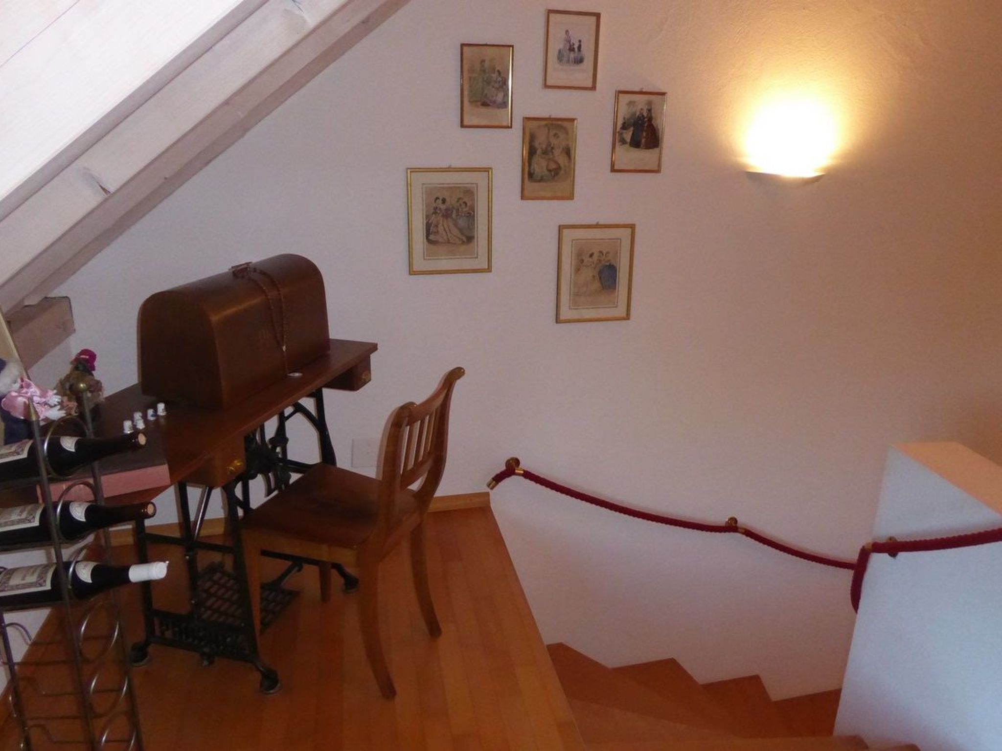 A room with a wooden desk, chair, and a red rope barrier. There are framed pictures on the wall and a light fixture.