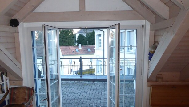 Una stanza con un'ampia porta vetrata che dà su un balcone con vista su edifici e alberi.