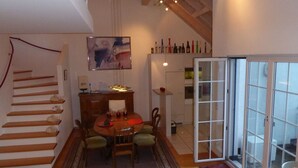 Zona pranzo con tavolo in legno, sedie e tappeto. A sinistra, una scala; a destra, una porta scorrevole in vetro.