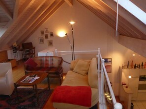 A cozy loft-style living room with a high ceiling, wooden beams, a sofa, a coffee table, and a floor lamp. - Haus Gaschür, (Bad Ragaz), by Interhome (Bad Ragaz)