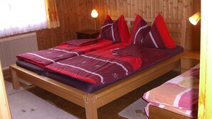 Ein hölzernes Bett mit roter Bettwäsche, ein Holz-Kopfstück und ein Nachttisch mit Lampe.
