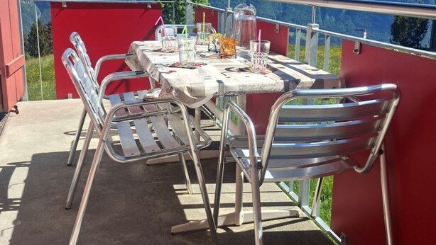 Eine Terrasse mit Esstisch, Metallstühlen und einer roten Wand.