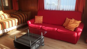 Ein Zimmer mit einem roten Sofa, einem Glastisch, einer gemusterten Decke und einem gerahmten Bild an der Wand.