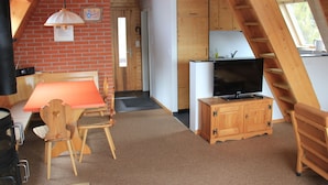 Een gezellige kamer met een eettafel, stoelen, een televisie, een houten kast en een trap.