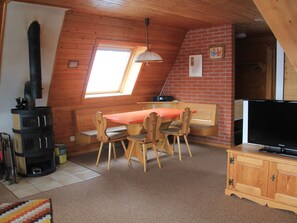 Une pièce chaleureuse avec un plafond en bois, une table à manger avec des chaises, un téléviseur et une cheminée.