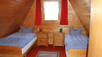Ein gemütliches Schlafzimmer im Dachgeschoss mit zwei Holzbetten, einem kleinen Tisch und einem Fenster mit roten Vorhängen.