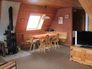 A cozy room with a sloped ceiling, a fireplace, a dining table with chairs, a television, and a small window.