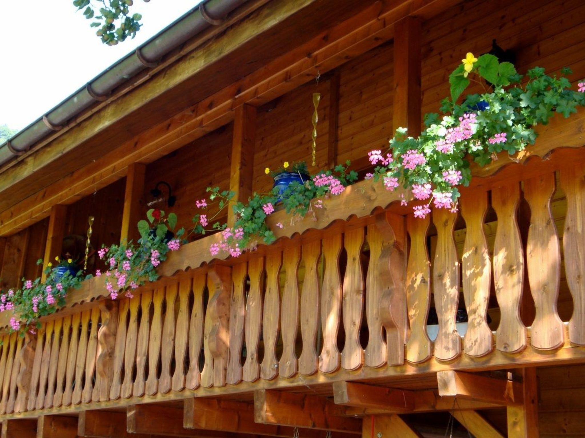 A wooden balcony with a decorative railing and hanging flower baskets.