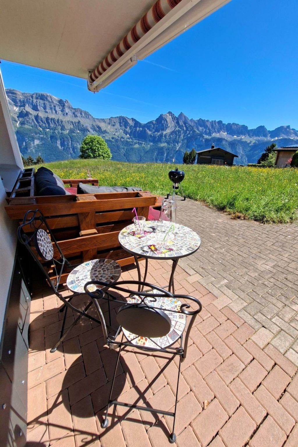 Un espacio al aire libre con vistas a montañas, una parrilla y una mesa con una bebida.