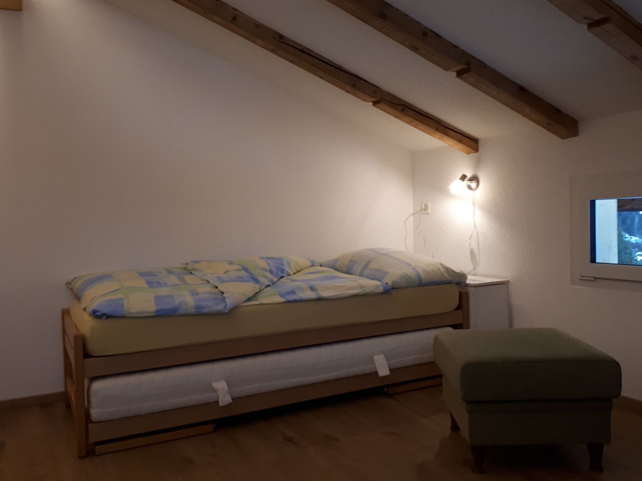 A single bed with a quilt, a bedside table with a lamp, and a window.