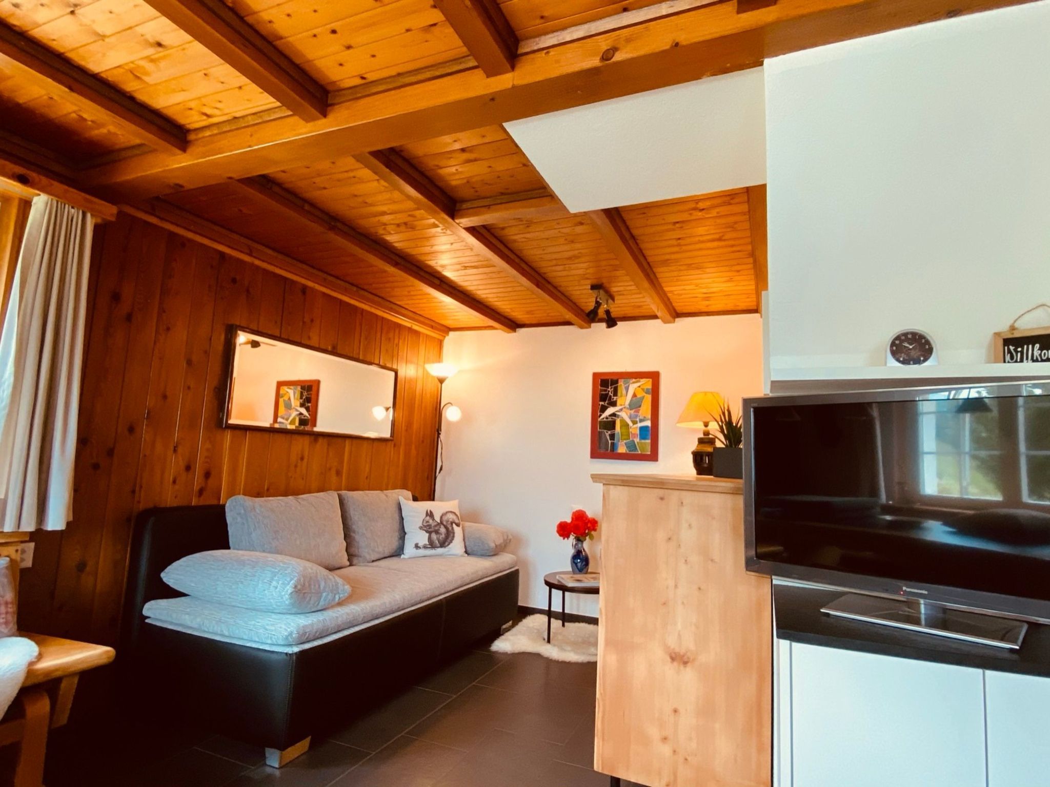 A cozy room with a sofa, a small table with a lamp, a painting, and a kitchen area with a stove.