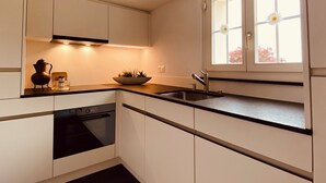 Een moderne keuken met witte kastjes, een zwart aanrecht, een ingebouwde oven en een raam met bloemversiering.