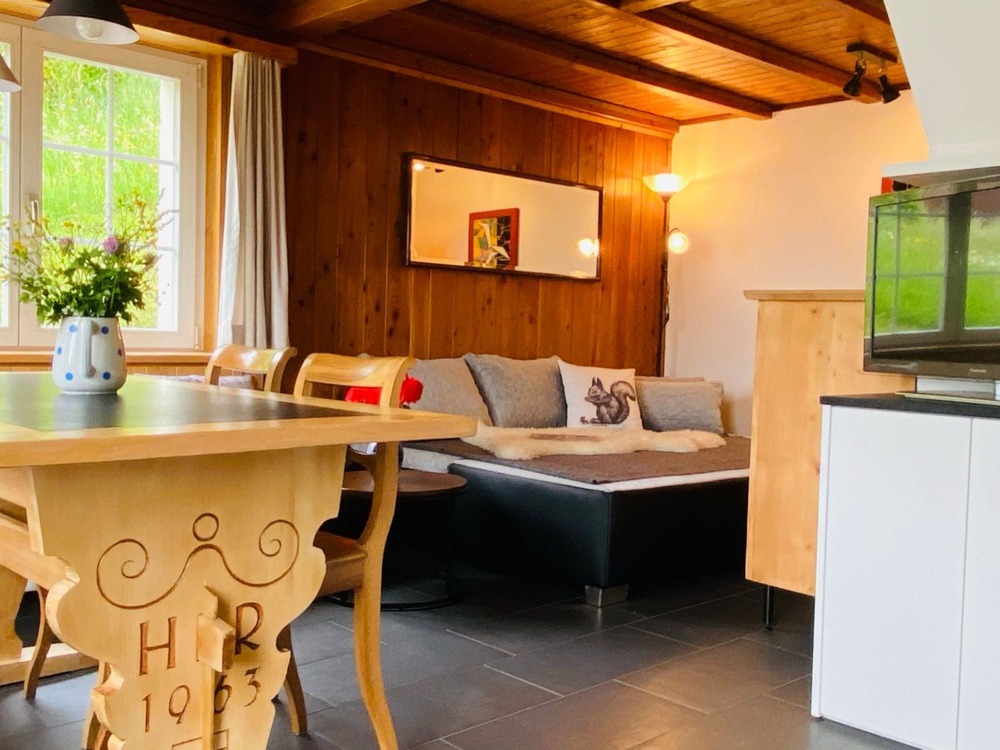 Una habitación acogedora con una mesa de madera, un sofá con cojines, un televisor y una ventana con cortinas.