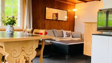 Una habitación acogedora con una mesa de madera, un sofá con cojines, un televisor y una ventana con cortinas.